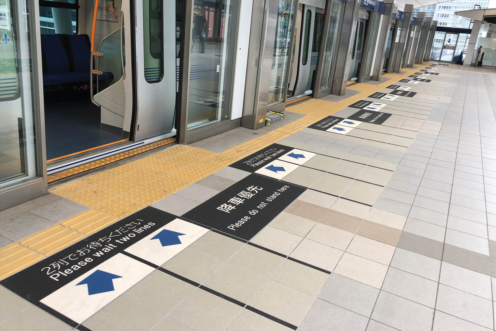 新橋駅のホームに施工された「2列でお待ちください」と表示されたハイブリッドストーン アベイラス アンプロップを電車のドアが状態で左斜から見た様子