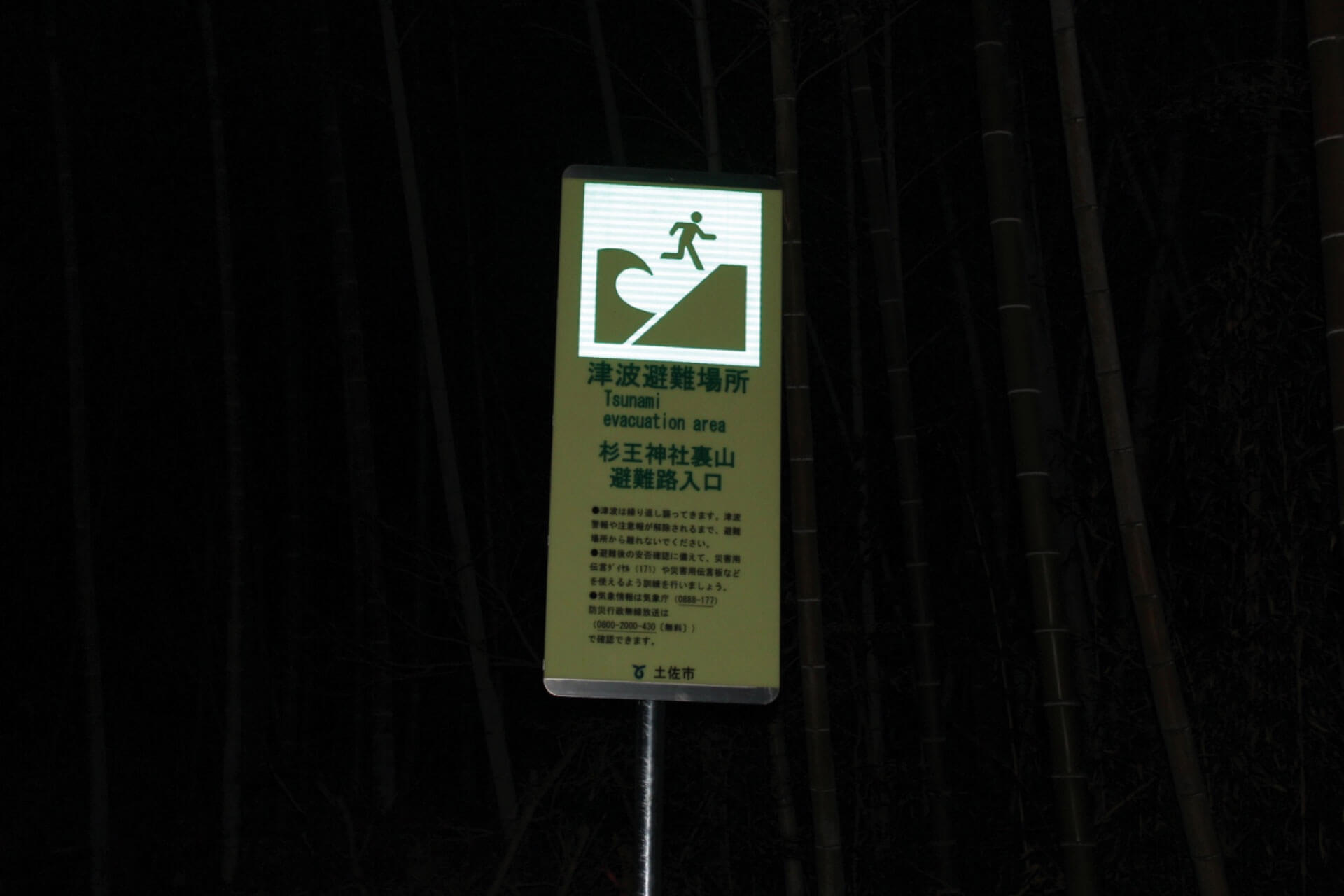 高知県土佐市の住宅地に設置されている杉王神社裏山避難路入口と表記されたアベイラス アルシオール サインプレート（高輝度蓄光式屋外用案内標示板）の再帰反射した状態