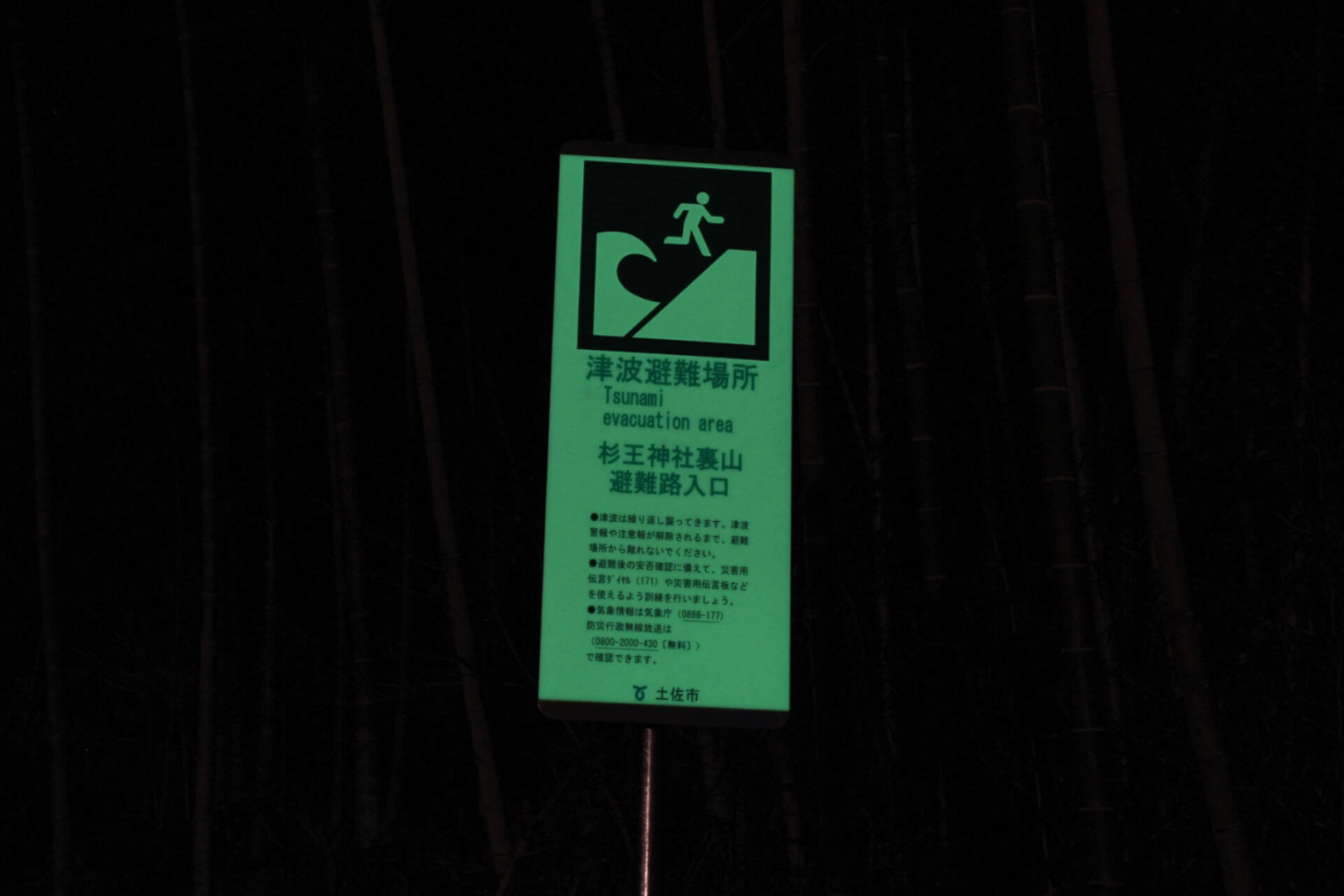 高知県土佐市の住宅地に設置されている杉王神社裏山避難路入口と表記された暗視下のアベイラス アルシオール サインプレート（高輝度蓄光式屋外用案内標示板）
